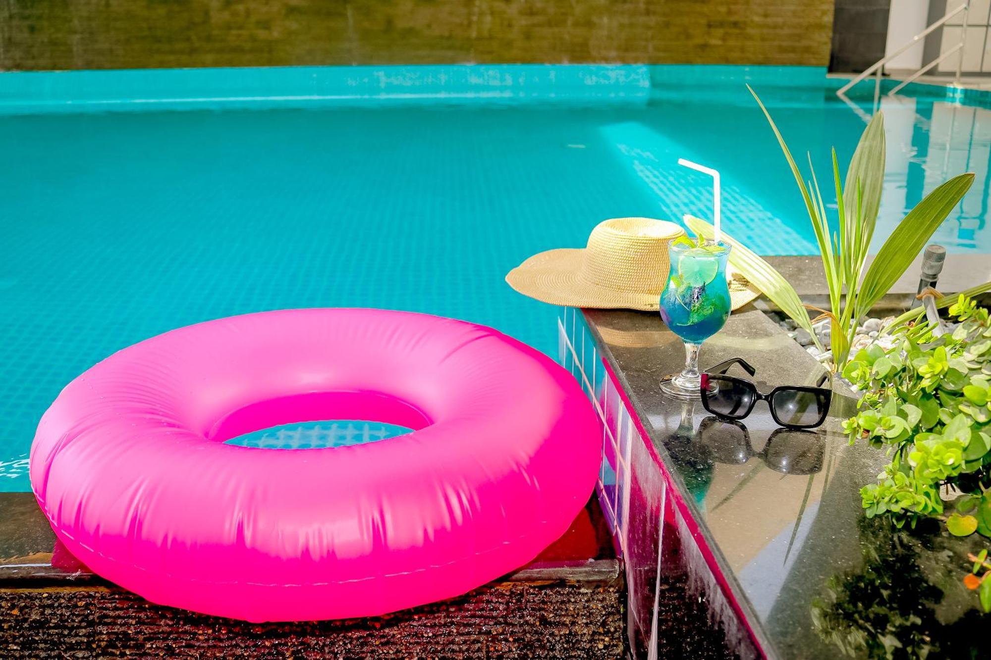 Lagoona Beach Luxury Resort And Spa Manama Exterior foto The photo shows a vibrant and inviting scene by a swimming pool. In the foreground, there is a large pink inflatable float and a stylish straw hat. Next to the float, a refreshing cocktail in a glass is displayed, complete with a straw and garnishes.