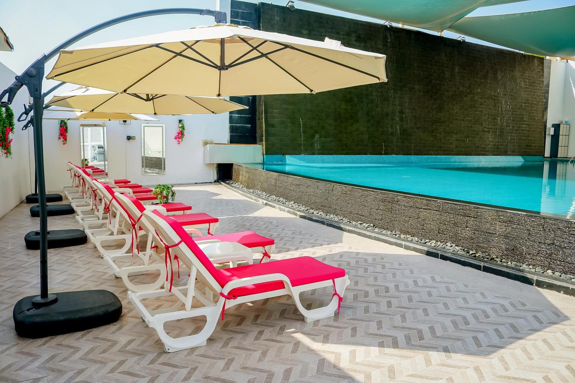 Lagoona Beach Luxury Resort And Spa Manama Exterior foto The photo shows a sunny poolside area with several lounge chairs arranged in a row. Each chair features red cushions and is positioned under large, beige umbrellas for shade. In the background, there is a beautiful swimming pool with clear blue water