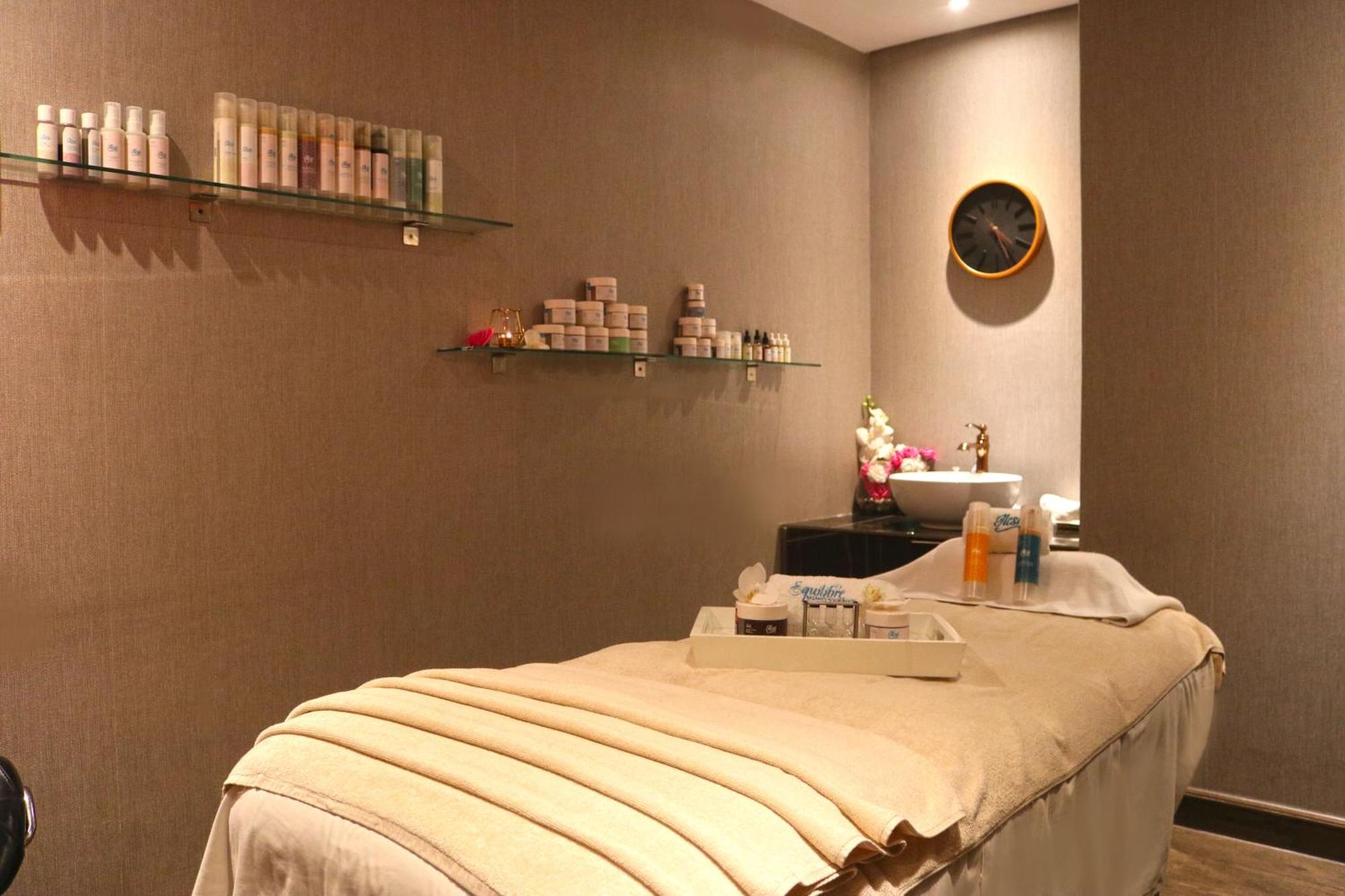Lagoona Beach Luxury Resort And Spa Manama Exterior foto The photo shows a spa treatment room. There is a massage table draped with a light-colored blanket, creating a relaxing atmosphere. On the wall, there are shelves displaying various skincare products in bottles and jars. A clock is mounted on the wal