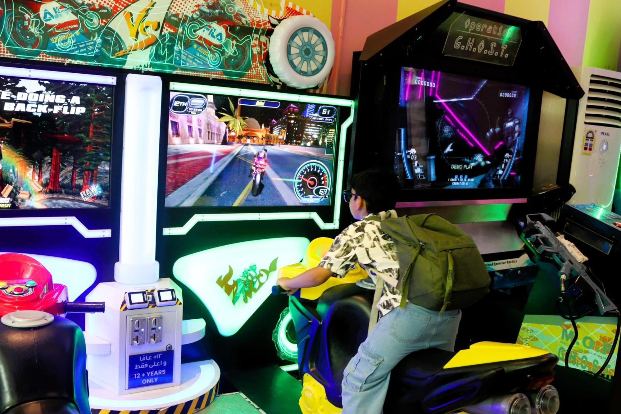 Lagoona Beach Luxury Resort And Spa Manama Exterior foto The photo shows a person playing an arcade motorcycle racing game. They are seated on a motorcycle-shaped seat, actively engaging with the game displayed on the screen in front of them. The screen shows a vibrant racing scene with streets and colorfu