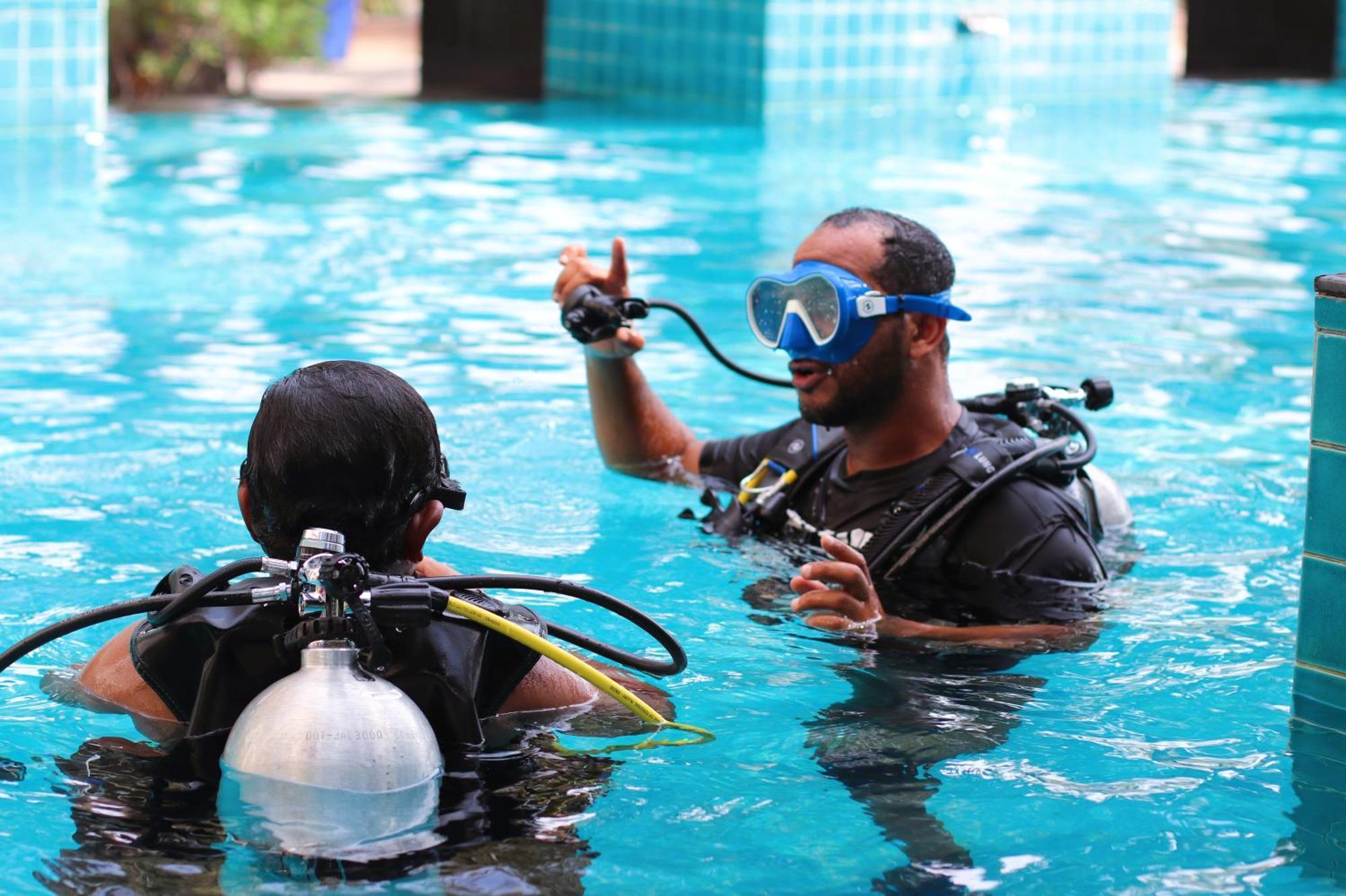 Lagoona Beach Luxury Resort And Spa Manama Exterior foto The photo shows two divers in a pool. One diver is wearing a scuba mask and is speaking to the other diver, who is also equipped with scuba gear. They appear to be engaged in a discussion, possibly related to diving instructions or safety. The water 