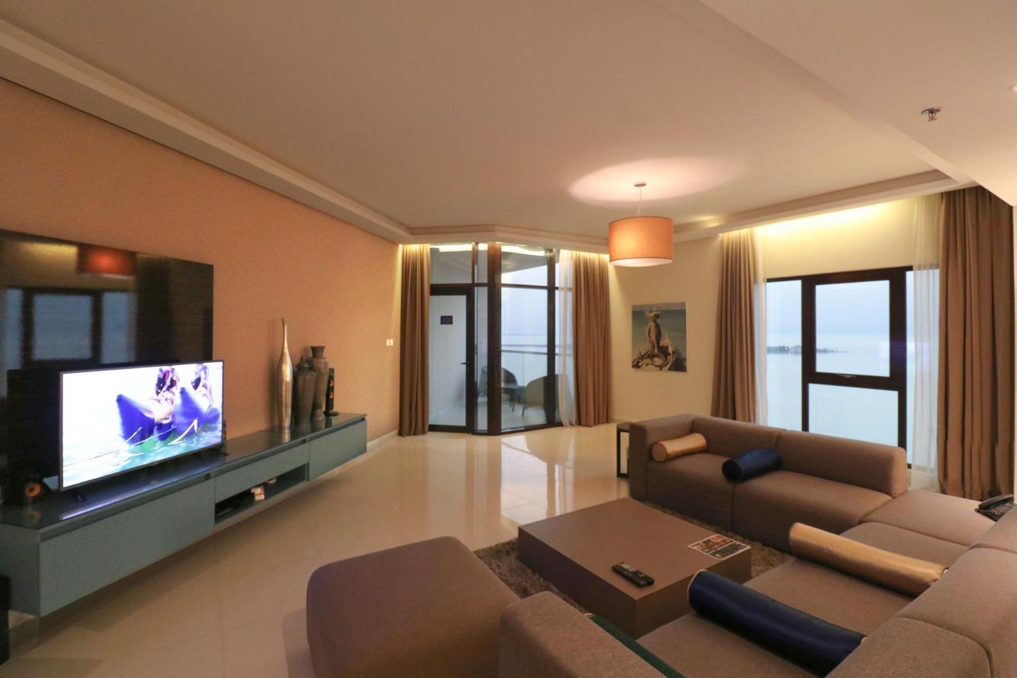 Lagoona Beach Luxury Resort And Spa Manama Exterior foto The photo shows a modern living room with a sleek design. There is a large wall-mounted television on a contemporary entertainment unit, with decorative items placed beside it. The room features a comfortable sectional sofa in light tones, with a cof