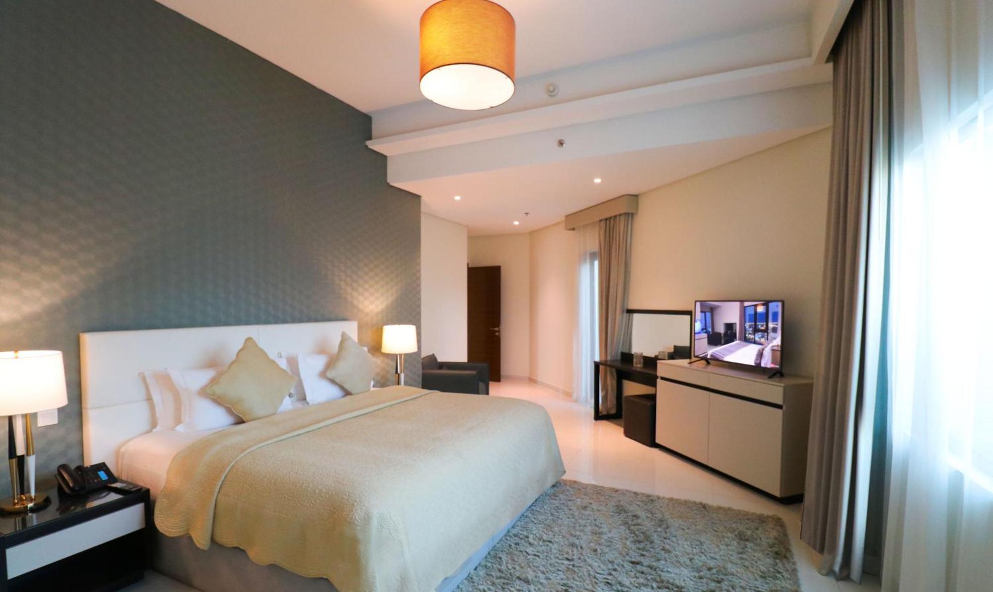 Lagoona Beach Luxury Resort And Spa Manama Exterior foto The photo shows a modern hotel room featuring a large bed with a light-colored blanket and decorative pillows. The walls are painted in a subtle shade, and there is a textured accent wall behind the bed. On one side, a bedside lamp provides warm ligh