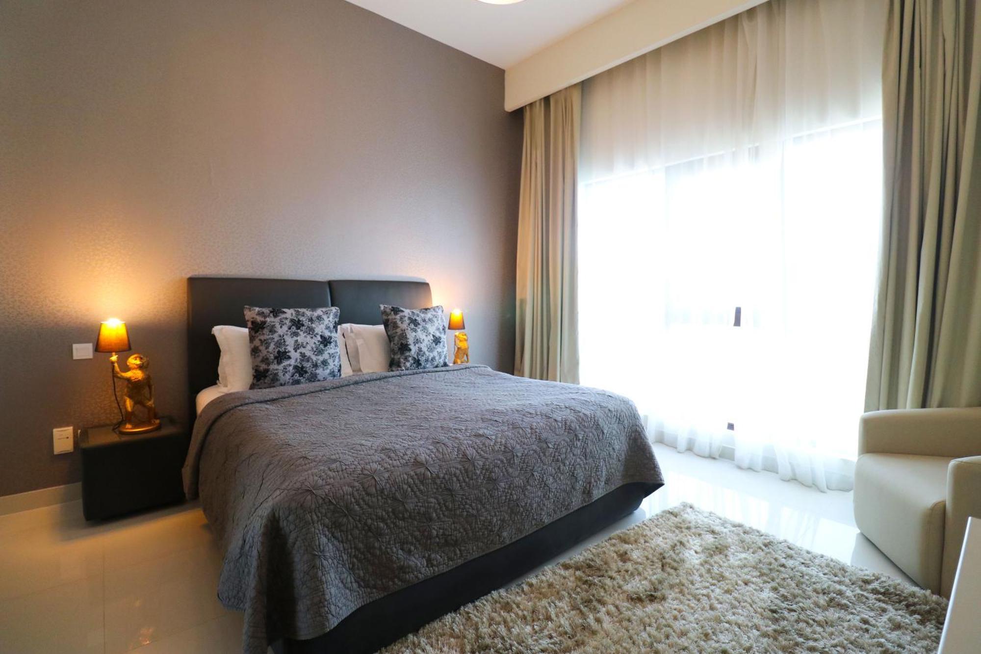 Lagoona Beach Luxury Resort And Spa Manama Exterior foto The photo shows a stylish bedroom with a modern design. It features a large bed with a dark gray bedspread and decorative pillows. On either side of the bed are two wooden nightstands, each with a lamp. There is a large window covered with light, flo